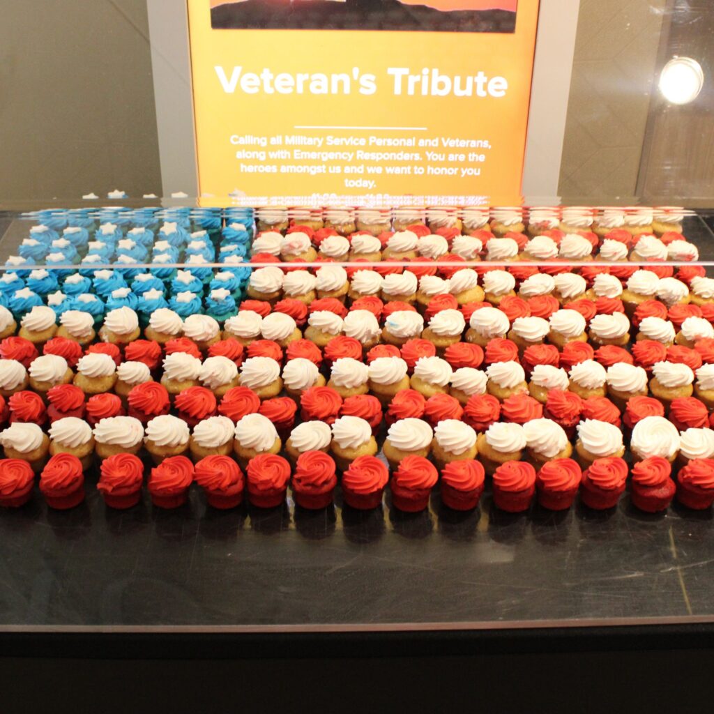 A display of cupcakes arranged in the shape of the American flag, featuring red, white, and blue frosting, with a sign above that reads "Veteran's Tribute."