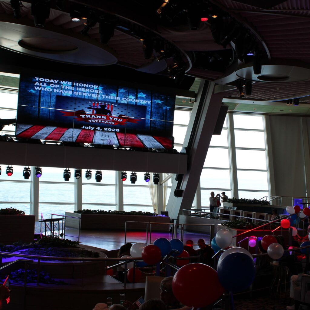 A large screen displaying a message of honor, with an audience and decorations in a spacious venue.