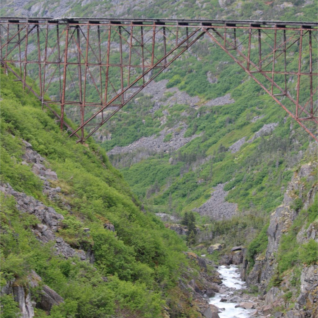 A wooden trestle bridge surrounded by dense greenery and mountains.

