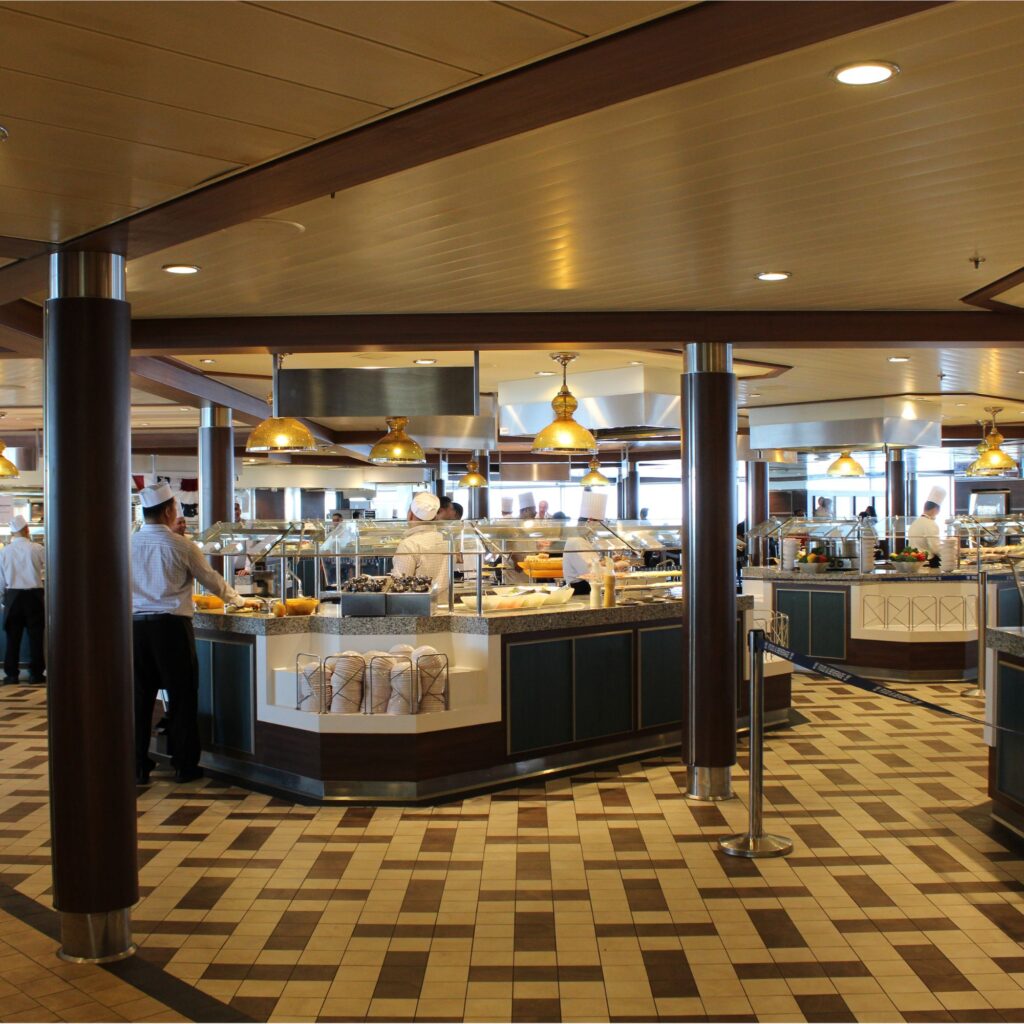 A well-lit buffet featuring food stations, serving staff, and a varied selection of dishes displayed in warming trays.
