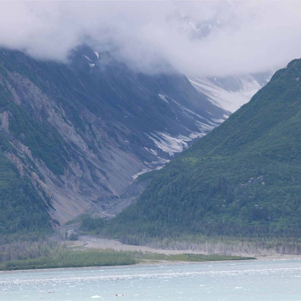 A mountainous landscape with green hills, rocky slopes, and a partially cloudy sky.