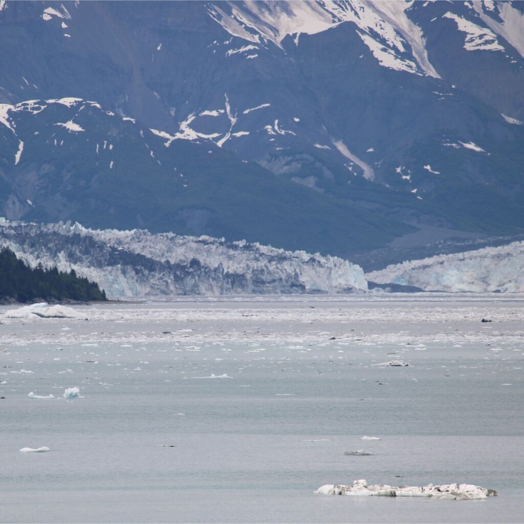 A scenic landscape featuring a body of water with icebergs, surrounded by mountainous terrain and glaciers in the background.