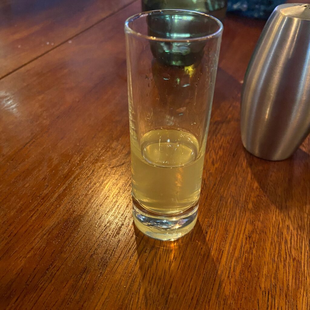 A shot glass filled with a light-colored liquid, placed on a wooden table.

