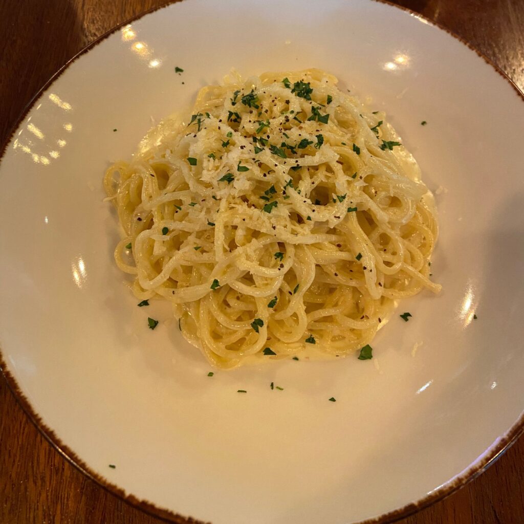 A plate of carbonara spaghetti topped with grated cheese and parsley.

