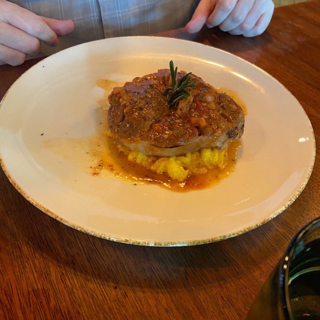 A plate of food featuring a piece of meat garnished with herbs, served over a bed of mashed potatoes.