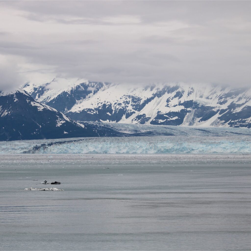 A landscape view of snowy mountains and glaciers along a calm body of water.