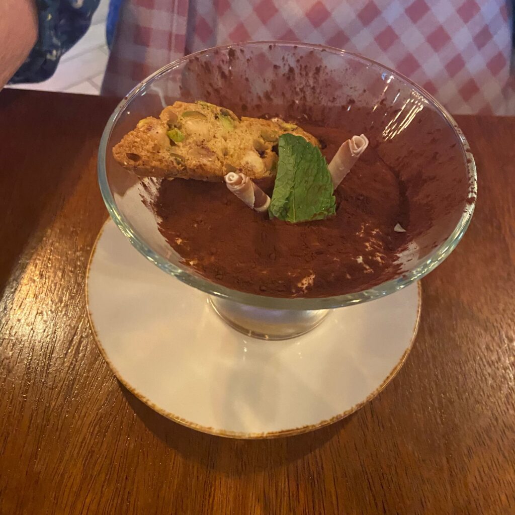 A dessert in a glass bowl with chocolate, a cookie on top, and a mint leaf for garnish.