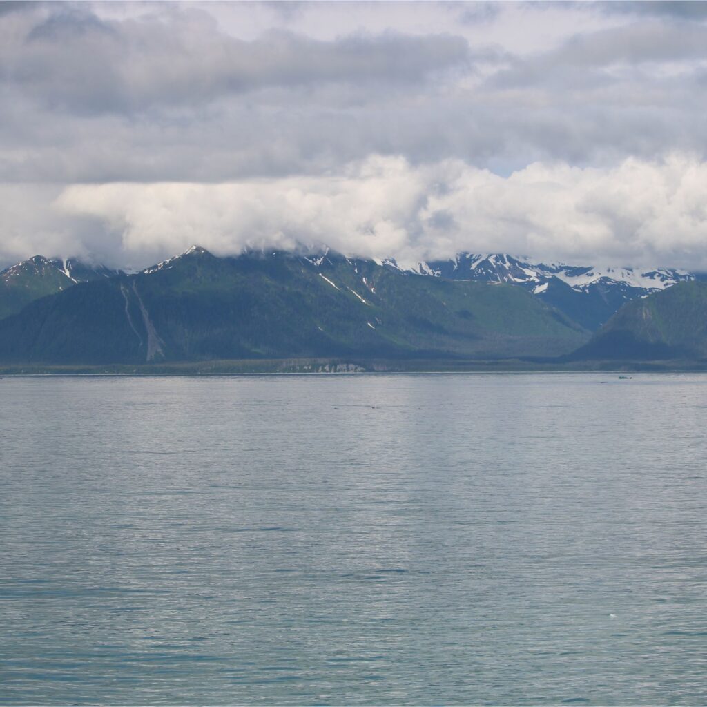 A scenic view of mountains covered in clouds along a tranquil body of water.

