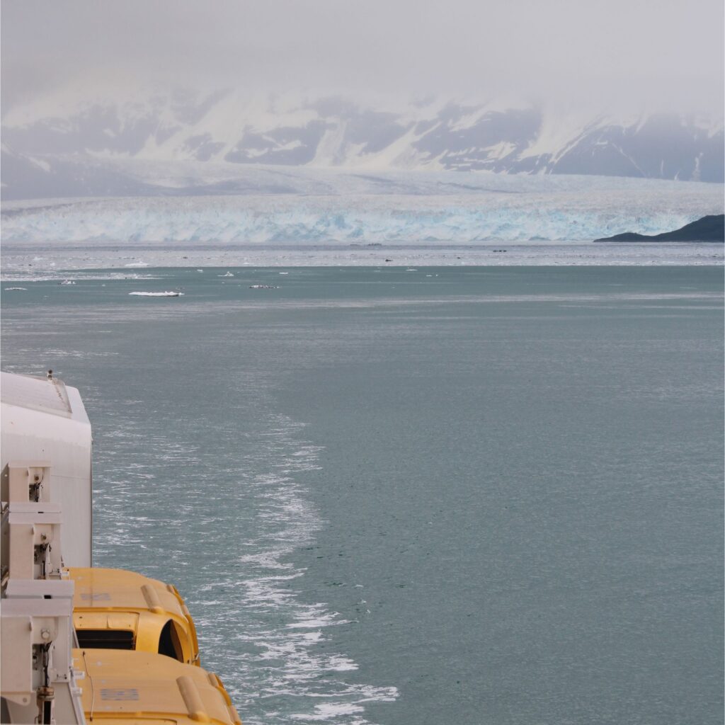A view of a glacier from a cruise ship. There is a icy landscape with water in the foreground.

