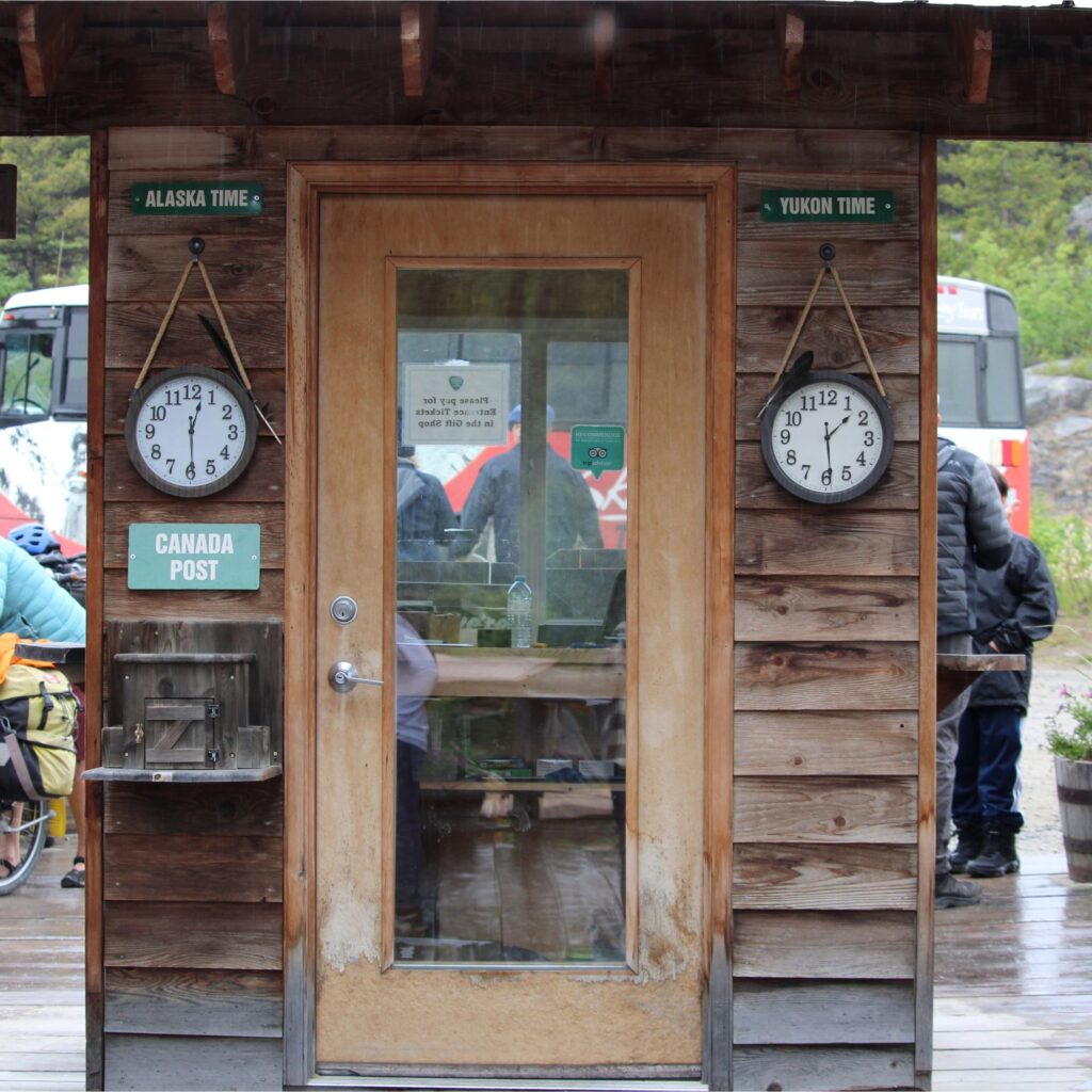 A small shed with a glass door and two clocks that tell the time for Alaska and Canada.