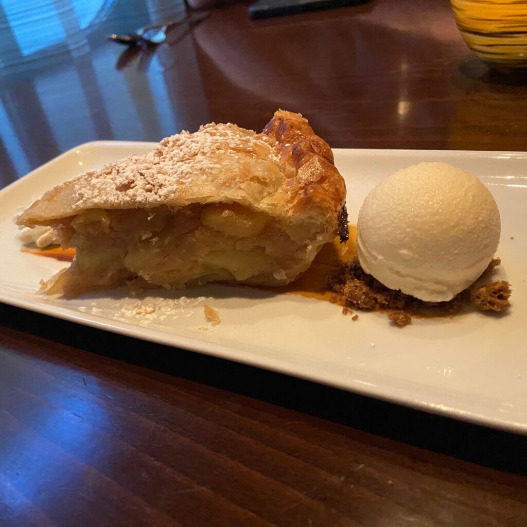 A slice of apple pie with a scoop of vanilla ice cream on the side, served on a white plate.