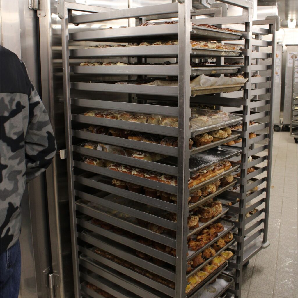 A metal rack filled with various baked goods, standing in a large kitchen.