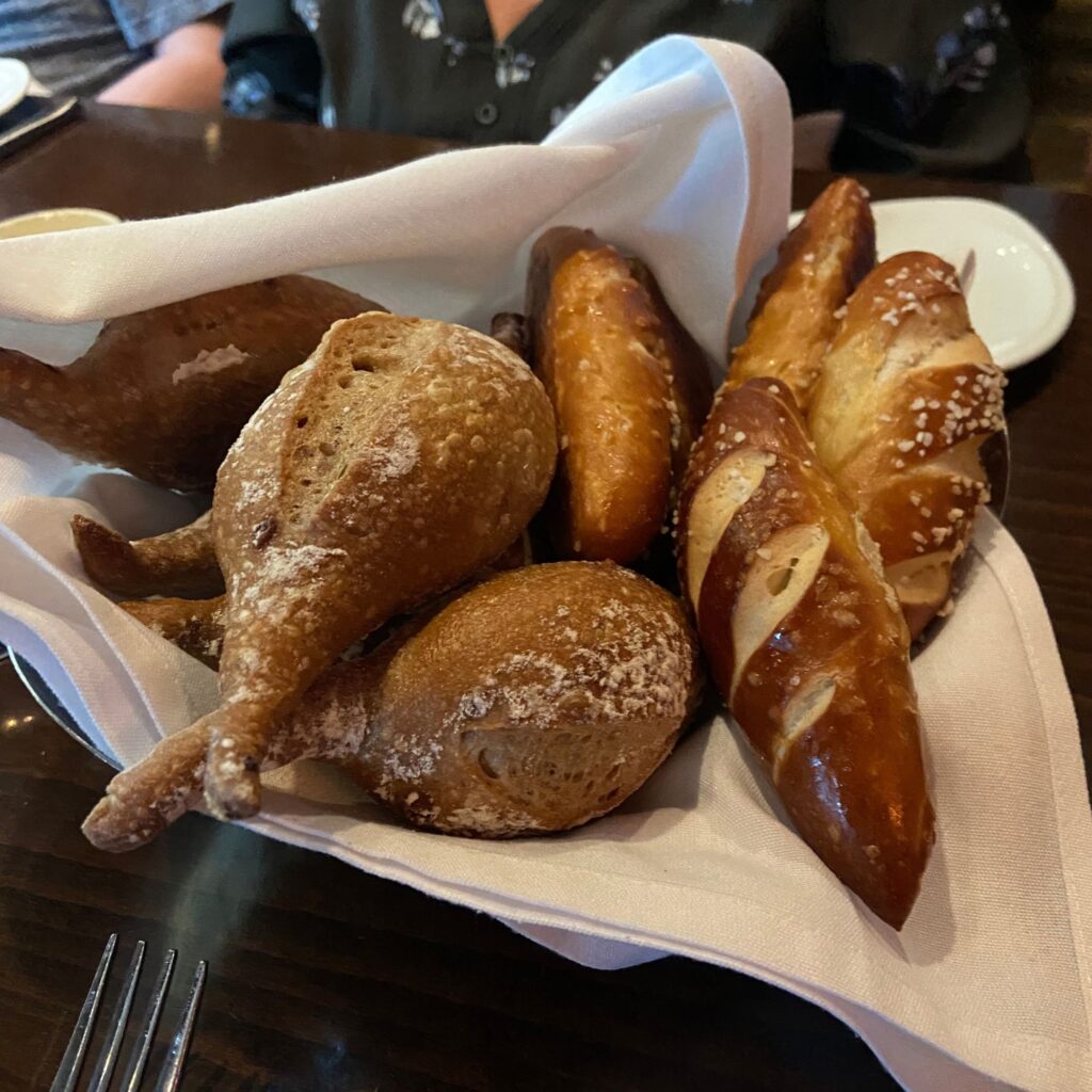 A basket of assorted baked goods, including bread and pretzel rolls, sitting on a table.