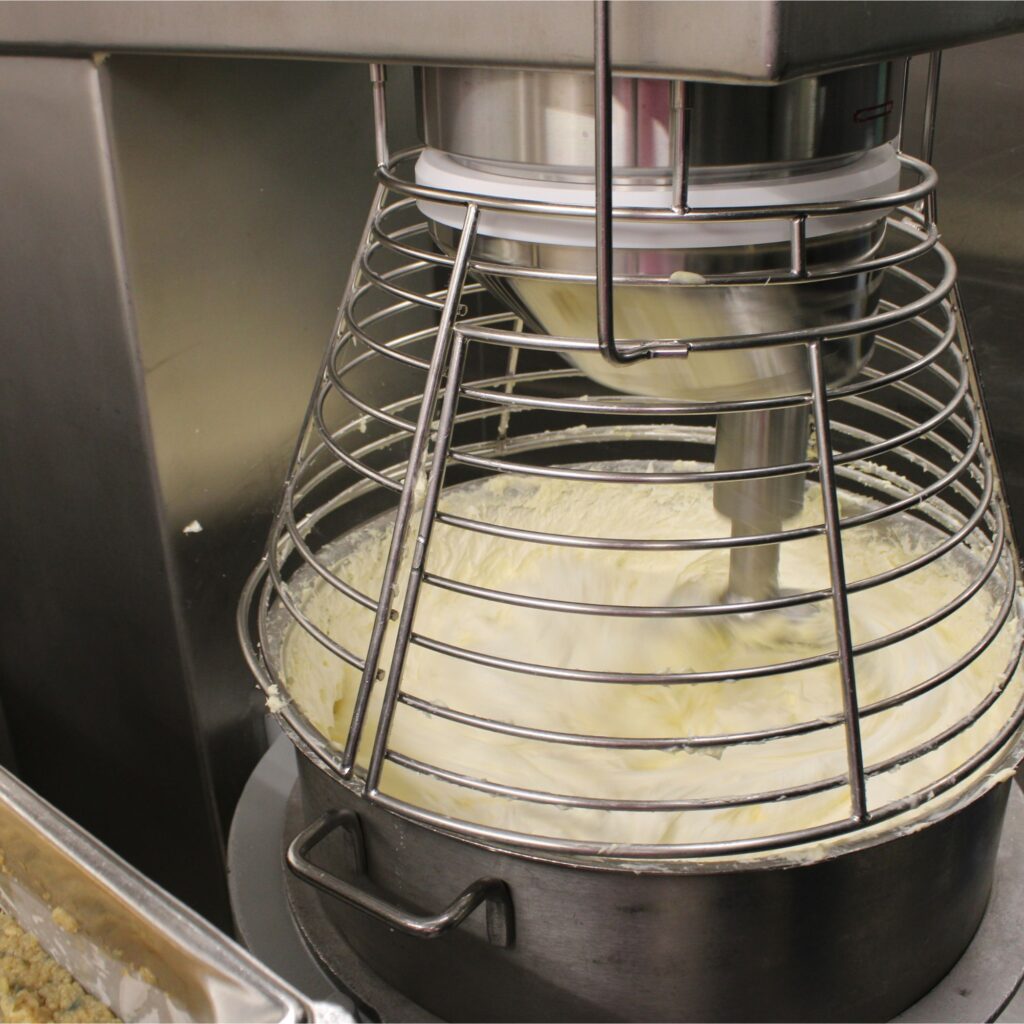 A large industrial mixer with a metal bowl containing a thick white mixture.