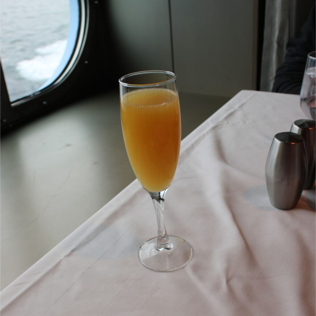 A flute of orange liquid on a table next to a window.
