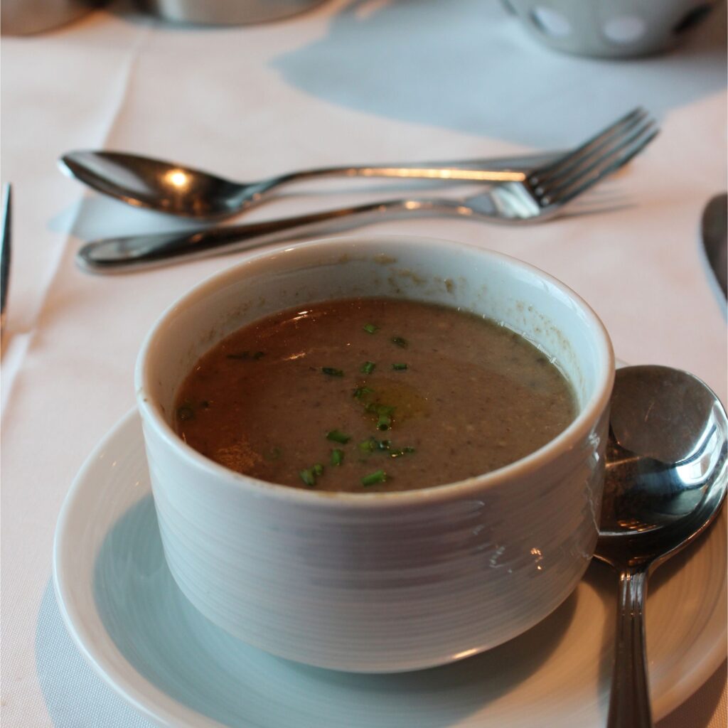 A bowl of soup with green herbs on top, placed on a white table setting with silverware.