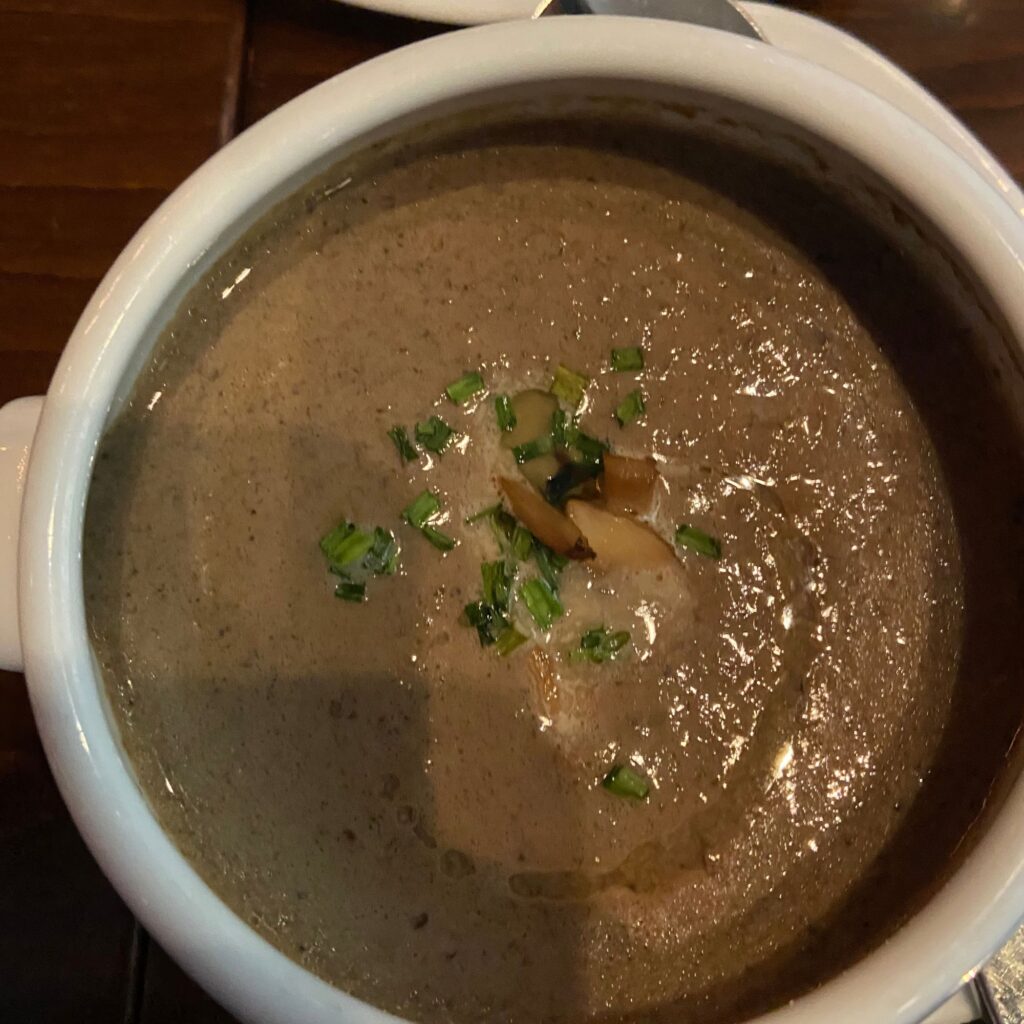 Up close of bowl of soup with green herbs and mushrooms on top.
