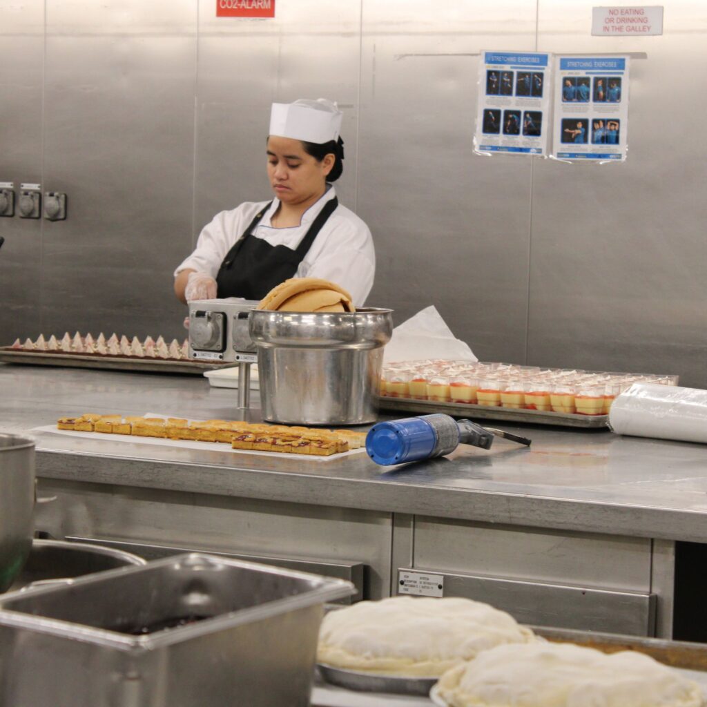 A chef in a kitchen preparing dishes, with trays of food arranged on a table.