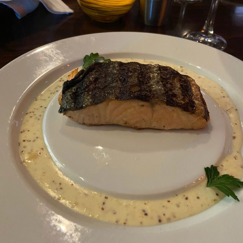 A piece of grilled fish on a white plate surrounded by a creamy white sauce