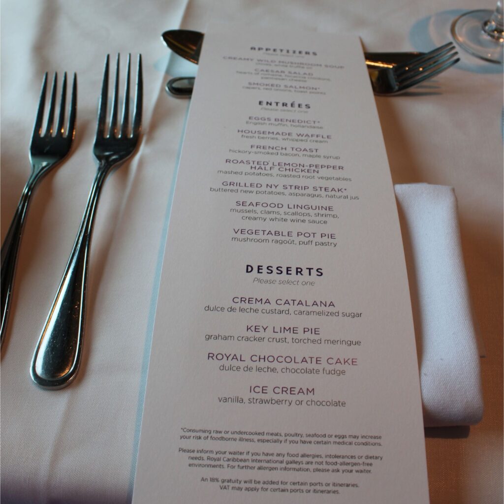 Menu with sections for appetizers, entrées, and desserts, listing various dishes including grilled strip steak, seafood linguine, crema catalana, and royal chocolate cake. Forks and a napkin are visible on the table.