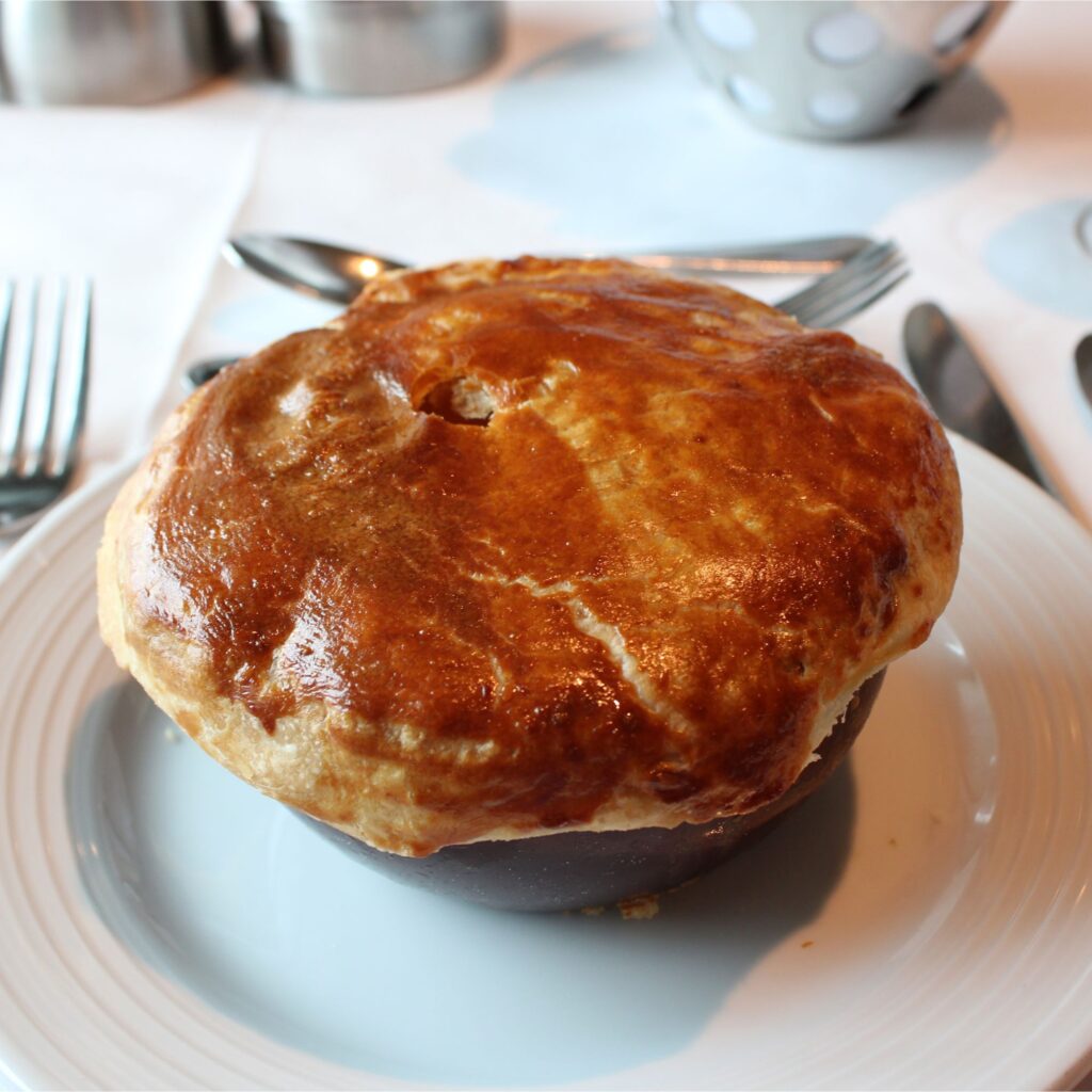 A golden-brown, flaky pastry pie on a white plate.
